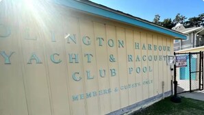 A wall with 'CLINTON HARBOR YACHT & RACQUET CLUB POOL' text, a gated entrance, and a clear sky. - Lily's Pad (Kill Devil Hills)