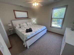 A bedroom with a bed, a ceiling fan, a window, and a nightstand. - Lily's Pad (Kill Devil Hills)