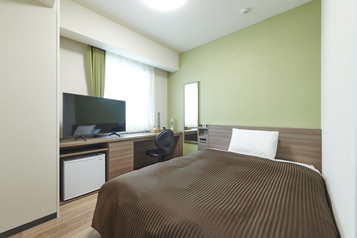 A hotel room with a bed, a desk with a computer, a television, and a small refrigerator.