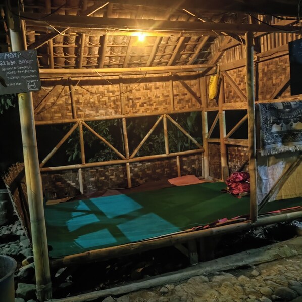 A bamboo structure with a green mat on the floor, a sign with text, and a woven ceiling.