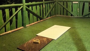 Quarto com andaimes de bambu verde, um quadro branco e um tapete marrom com um objeto triangular no chão.