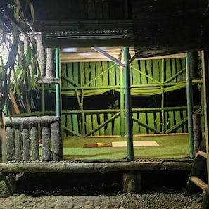 Un espacio al aire libre techado con una hamaca, un banco de madera y un sendero de piedra.