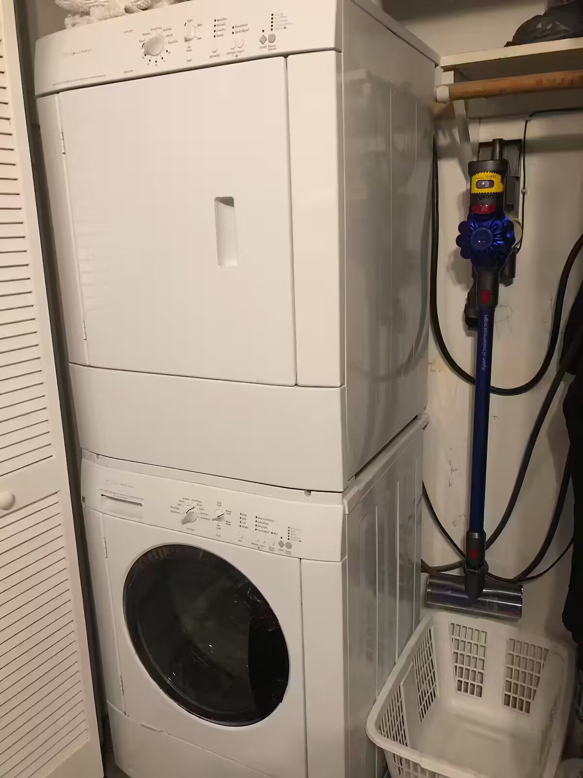 Un appareil combiné lave-linge et sèche-linge, ainsi qu’un aspirateur et un panier à linge.