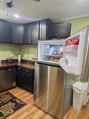 A kitchen with a stainless steel refrigerator, dark wooden cabinets, a dishwasher, and a trash bin. - Infinity Guest House - Corporate Housing (Sterlington)