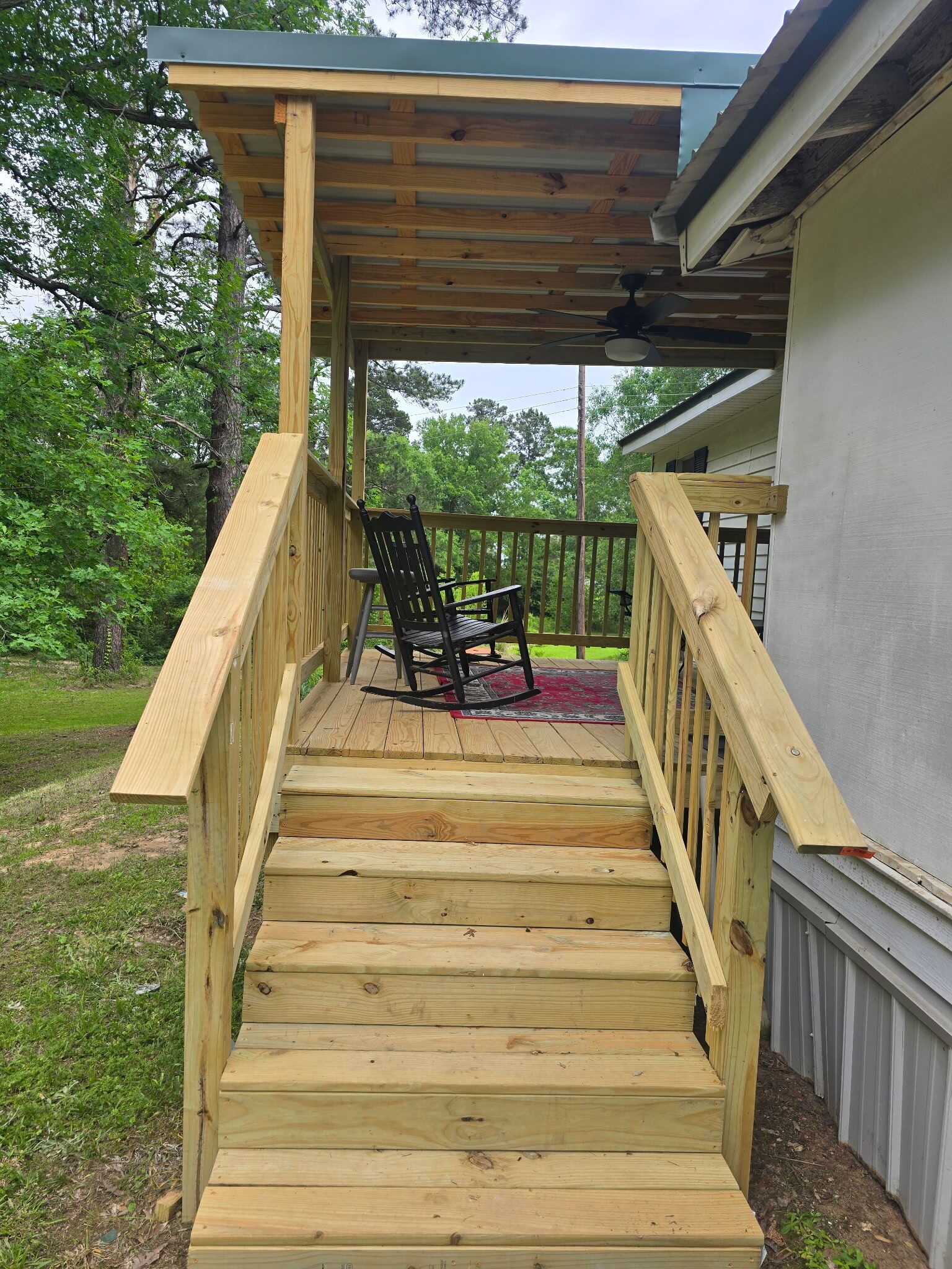 A wooden deck with a chair and a rug, leading to a covered porch area.