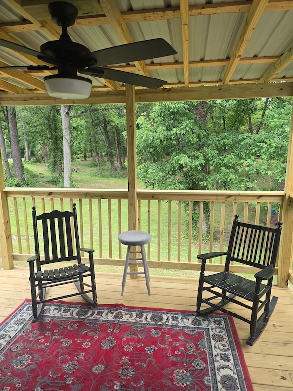 A covered outdoor area with two wooden chairs, a small stool, and a ceiling fan.