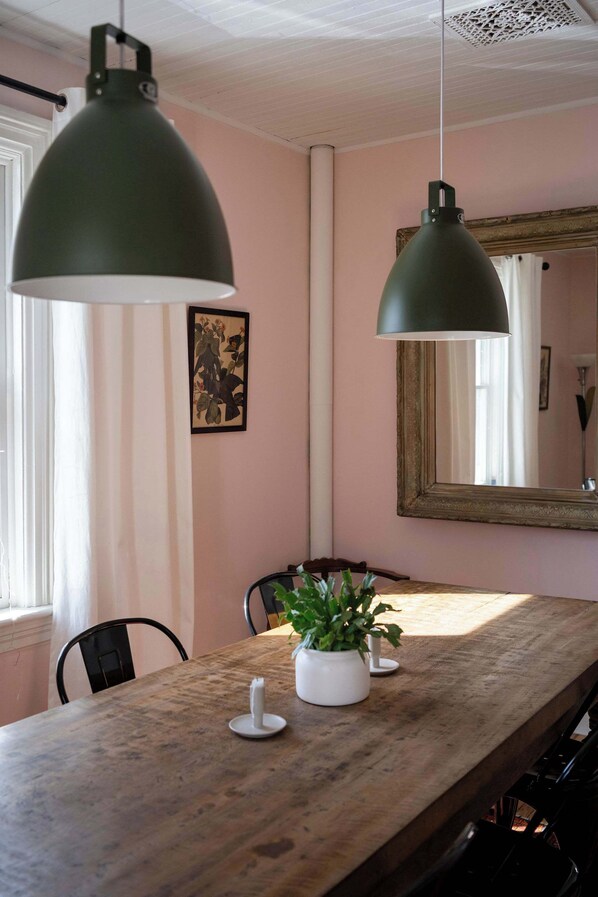 A dining area with a wooden table, two pendant lights, a potted plant, and a mirror on the wall.