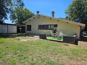 Une maison de plain-pied avec un patio, un petit jardin et une voiture garée devant.