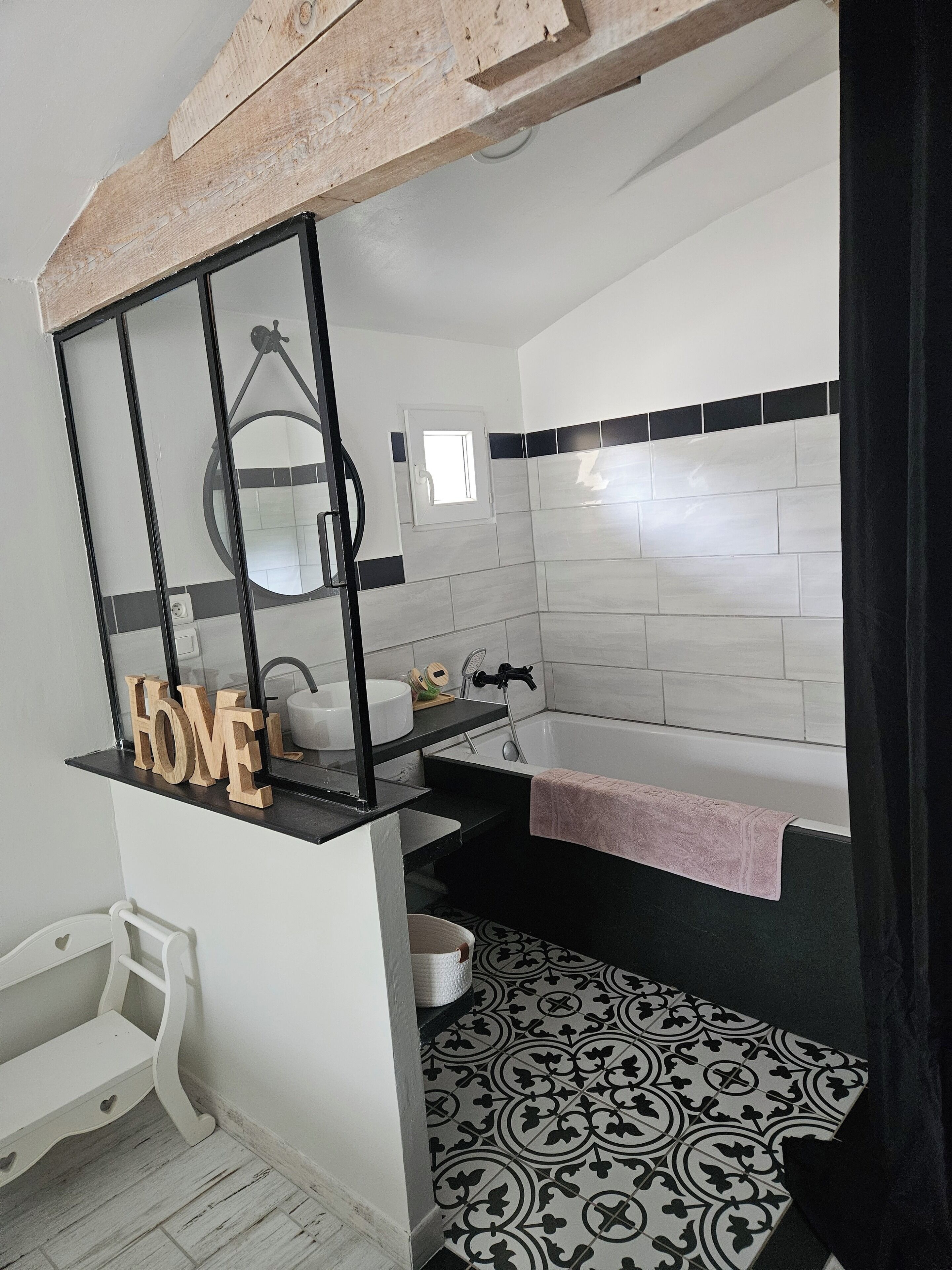 Un bagno con lavandino bianco, piano di lavoro nero e uno specchio. Un asciugamano è appeso alla vasca, e il pavimento presenta piastrelle decorate.