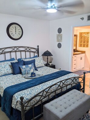 Ein Schlafzimmer mit Bett, Nachttischlampe, Wanduhr, Wanddekoration und einem durchgegangenen Tür sichtbaren Badezimmer.