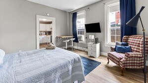 Ett sovrum med en säng, ett skrivbord, en stol, en tv och ett fönster med gardiner.