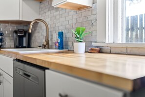 Eine Küche mit Holzarbeitsplatte, Spüle, Wasserhahn, einer Topfpflanze und einem Fenster.