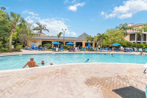 A swimming pool with lounge chairs and umbrellas, surrounded by palm trees and a building with a tiled roof. - Huge Family Condo at Bahama Bay, Balcony, Resort Amenities (Davenport)