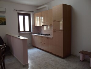 A compact kitchen with a gas stove, cabinets, and a window. - Agri Costella Country Hotel (Vieste)