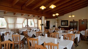 En restaurang med flera bord och stolar, synliga träbjälkar i taket och stora fönster med gardiner.
