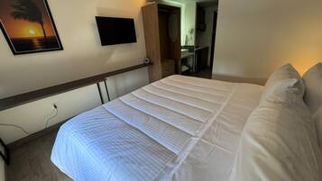 Une chambre d’hôtel avec un lit, une télévision, un tableau et un dressing.