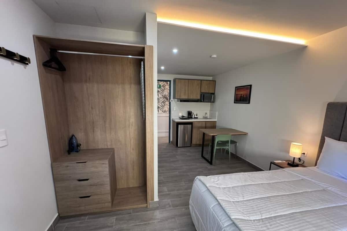 Ein Zimmer mit Bett, Schreibtisch, Küchenzeile und begehbarem Kleiderschrank.