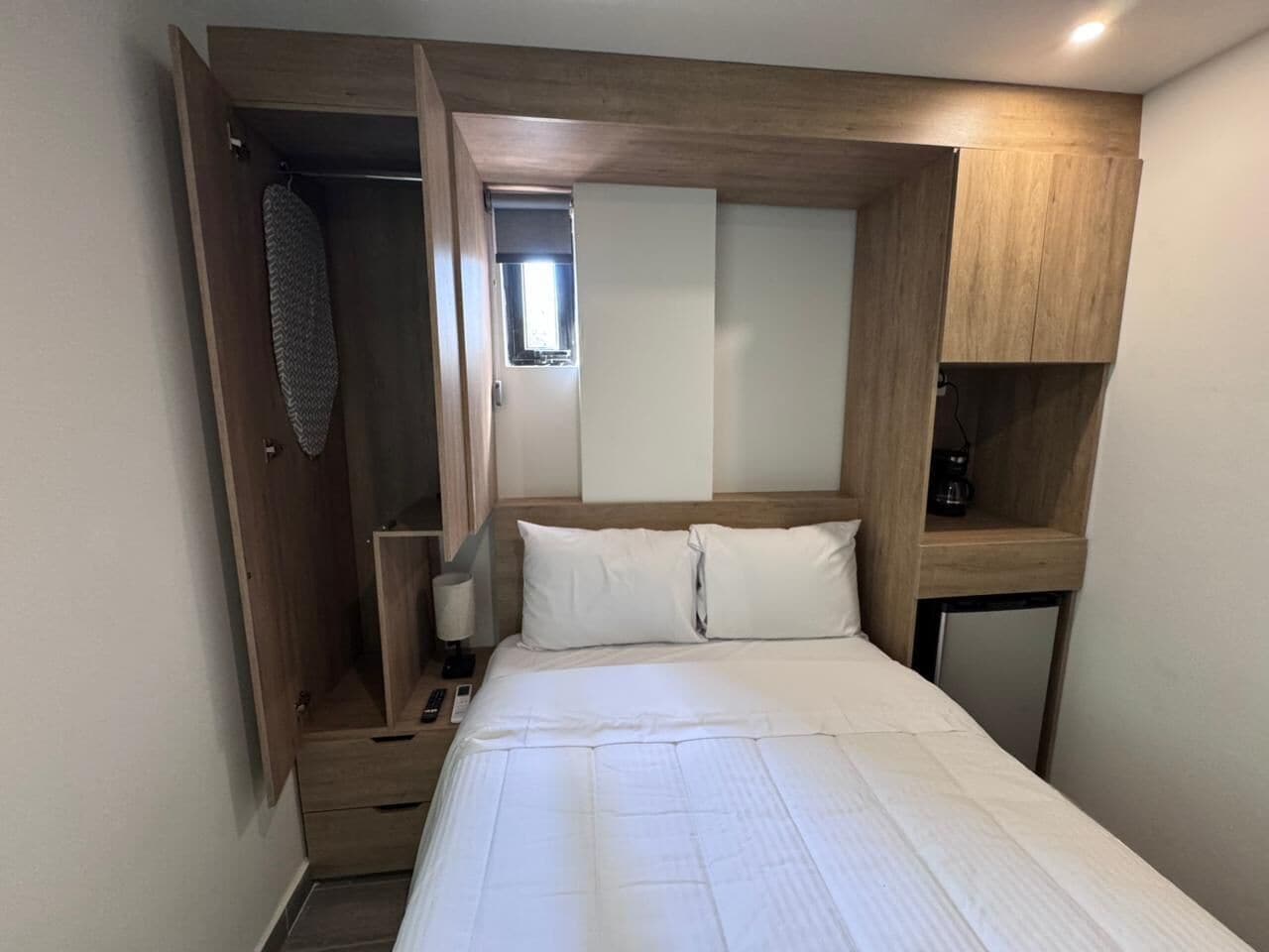 A bedroom with a bed, a wardrobe, a bedside table, a lamp, and a small shelf.