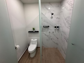 Une salle de bain moderne avec des toilettes, une douche Ă lâitalienne en verre, des murs en marbre et une petite Ă©tagĂšre contenant des articles de toilette.