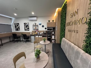 Un espace de bureau moderne comprenant un espace dâaccueil, un coin cuisine et un espace dĂ©tente avec un canapĂ© et des tables.