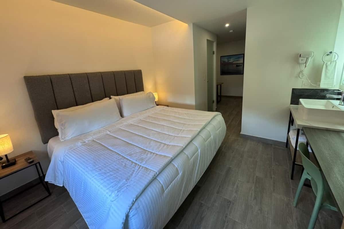 Ein Schlafzimmer mit Bett, Nachttisch, Lampe und Blick ins Badezimmer.