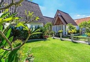Una propiedad residencial con un césped cuidado, una casa con techo de tejas y un jardín con diversas plantas.