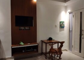 Una habitación con una televisión fijada en la pared, una mesita con una silla y una puerta con una toalla colgada.