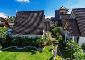Un edificio tradicional japonés con techo de tejas, rodeado por un jardín cuidado con diversas plantas y un sendero.