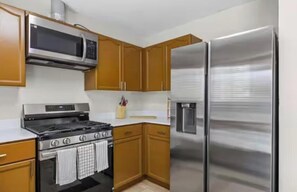 A kitchen with wooden cabinets, a stainless steel stove, a microwave, and a refrigerator. - ATX Hideout 3BR/2BA House (Austin)