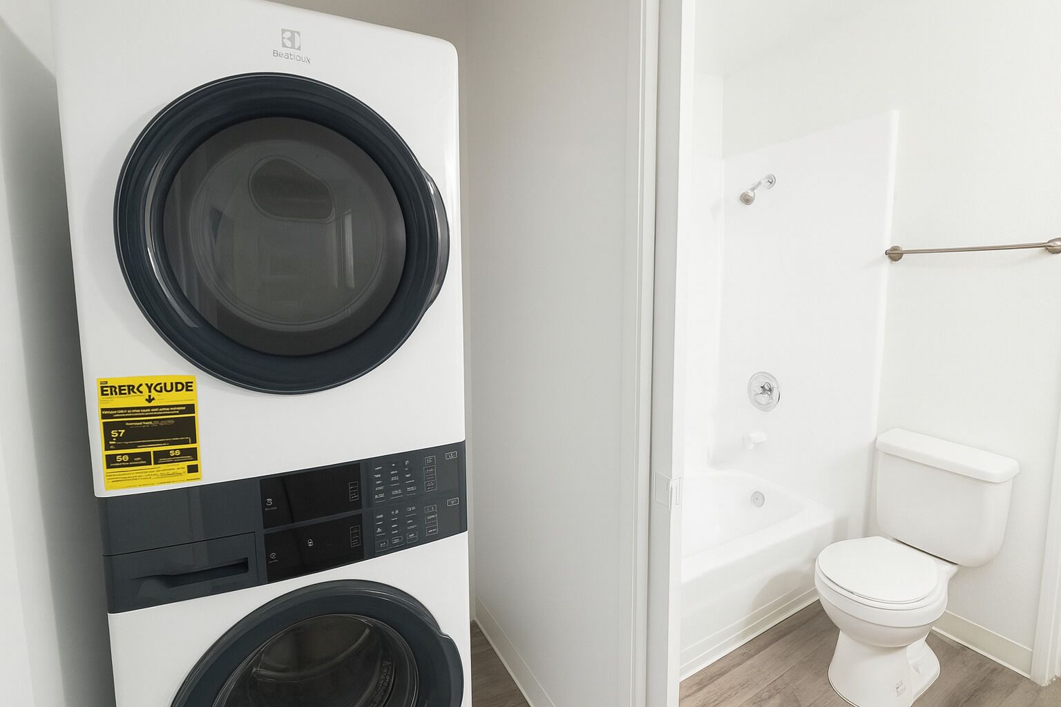 A compact, modern laundry room with a front-loading washer and dryer, a visible ENERGY GUIDE label, and a white toilet in the adjacent bathroom.