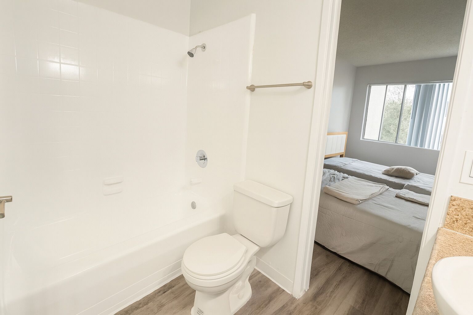 Ein Badezimmer mit Dusche, Toilette und einem durch eine offene Tür erkennbaren Bett.
