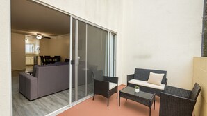 Un balcon avec une porte-fenêtre coulissante, un canapé, deux fauteuils, une petite table et une plante en pot.