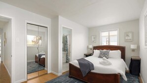 A hotel room with a large bed, a walk-in closet, a bathroom with a shower, and a window with blinds. - Golden Hour Overlook | Spa | In-Law Suite | Grill (San Diego)