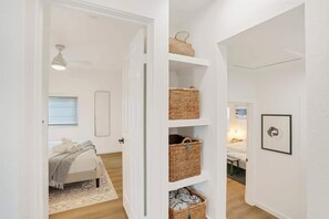 Ein Flur mit einem Bett, einer weißen Tür und einem an der Wand befestigten Regal mit Körben.