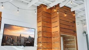 Una habitación con separador de madera, televisor montado mostrando un paisaje urbano y luces colgantes.