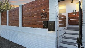 Un edificio con fachada de ladrillo blanco, paneles de madera y un conjunto de escaleras que llevan a una puerta.