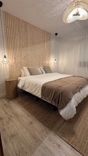 A bedroom with a bed, wooden panel wall, two pendant lights, and a round nightstand.