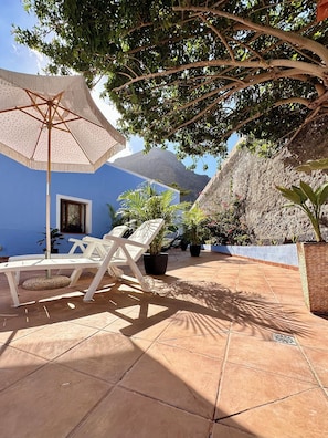 A patio with a white umbrella, white lounge chairs, potted plants, and a view of a mountain.