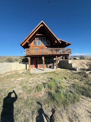 Une cabane en bois à deux étages, dotée d’un balcon, de fondations en pierre et surplombant un ciel dégagé.