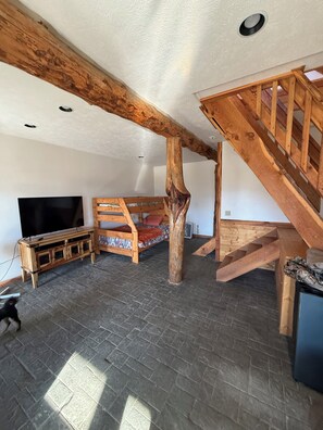 A loft-style room with exposed wooden beams, a bunk bed, a TV stand, and a staircase.