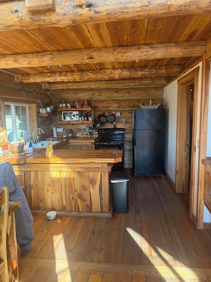 A rustic kitchen with wooden beams, a central island, a microwave, and a refrigerator.