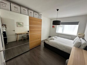 Ein Schlafzimmer mit Bett, Nachttisch, Schreibtisch, Stuhl und einem Fenster mit Blick.