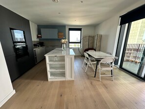 Eine moderne Küche mit einer zentralen Kochinsel, einem Essbereich mit Tisch und Stühlen und einem großen Fenster mit Ausblick.