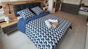A modern bedroom with a geometric-patterned wall, a wooden headboard, a neatly made bed with patterned bedding, a bedside table with a lamp, and a built-in wardrobe. - Apartment T3 of 83 M2 in Mâcon (Mâcon)