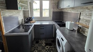A compact kitchen with a built-in stove, a washing machine, and a window with a view of buildings. - Apartment T3 of 83 M2 in Mâcon (Mâcon)