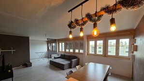 A modern living room with a large wooden dining table, a sofa, and a hanging light fixture. - Apartment T3 of 83 M2 in Mâcon (Mâcon)