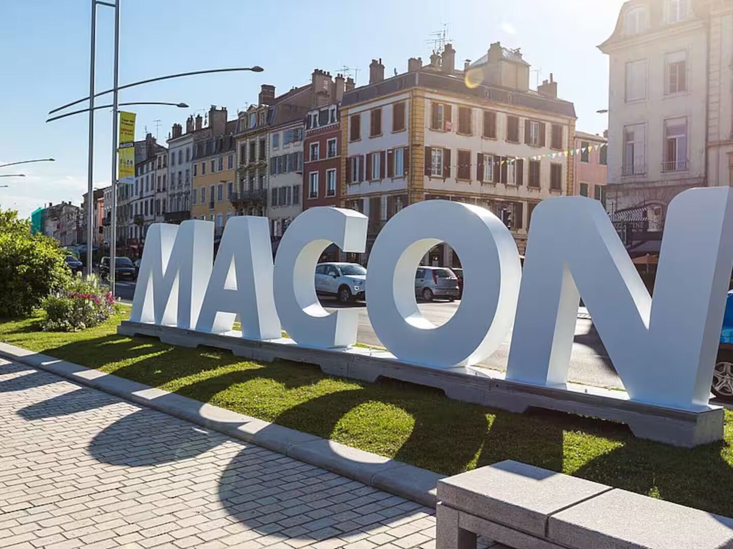 Een groot wit bord met de tekst 'MAGON' in hoofdletters, gelegen in een aangelegd gebied met gras en een verhard pad.