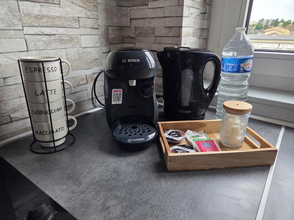 Un comptoir de cuisine avec une machine à café, une bouteille d’eau, un ensemble de tasses à café et un plateau contenant des dosettes de café.