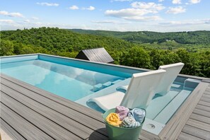 Una piscina con cubierta de madera, una silla y un balde de toallas.