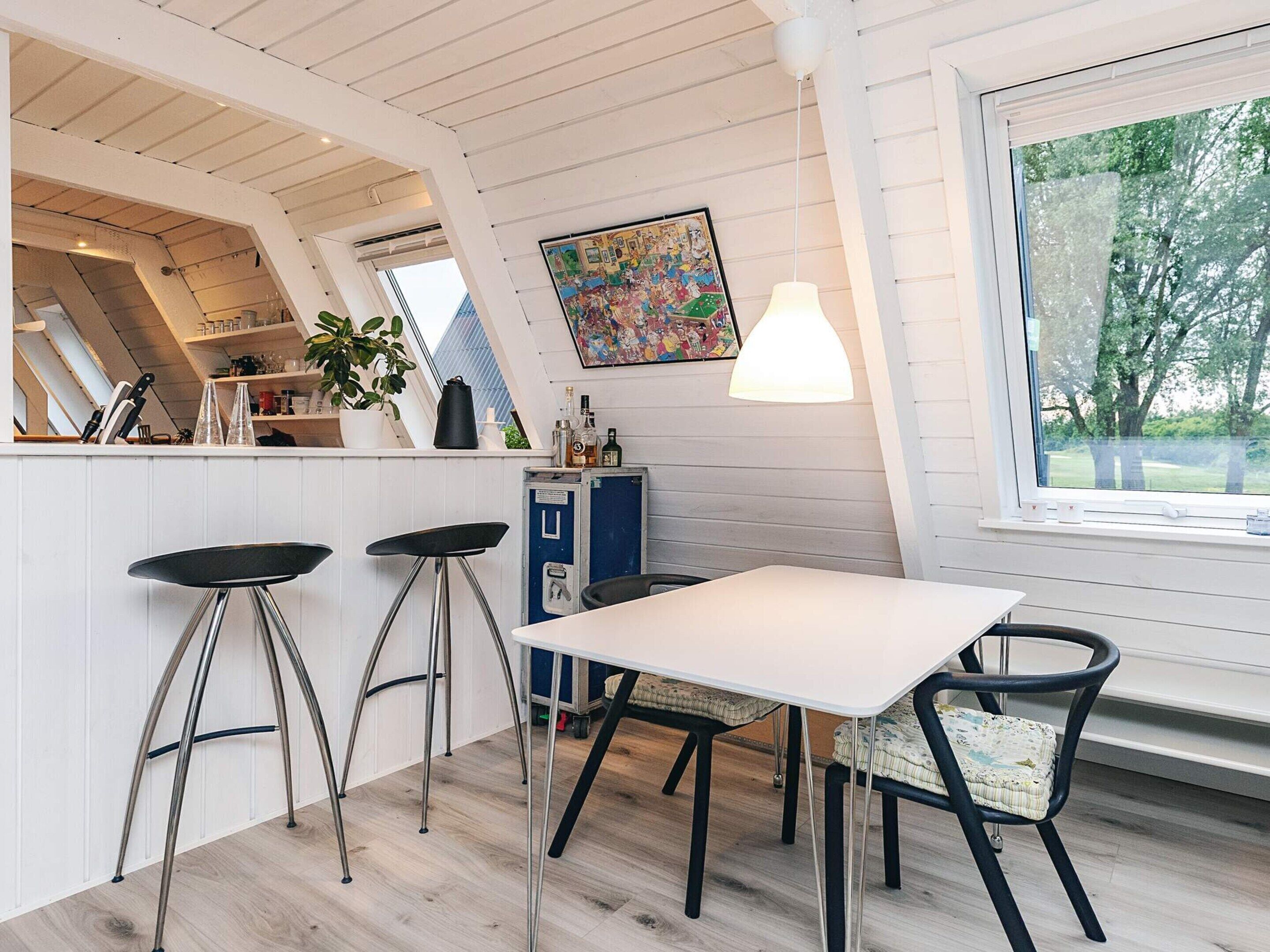 A kitchen with a white table, bar stools, a blue cabinet, and a window with a view of trees.